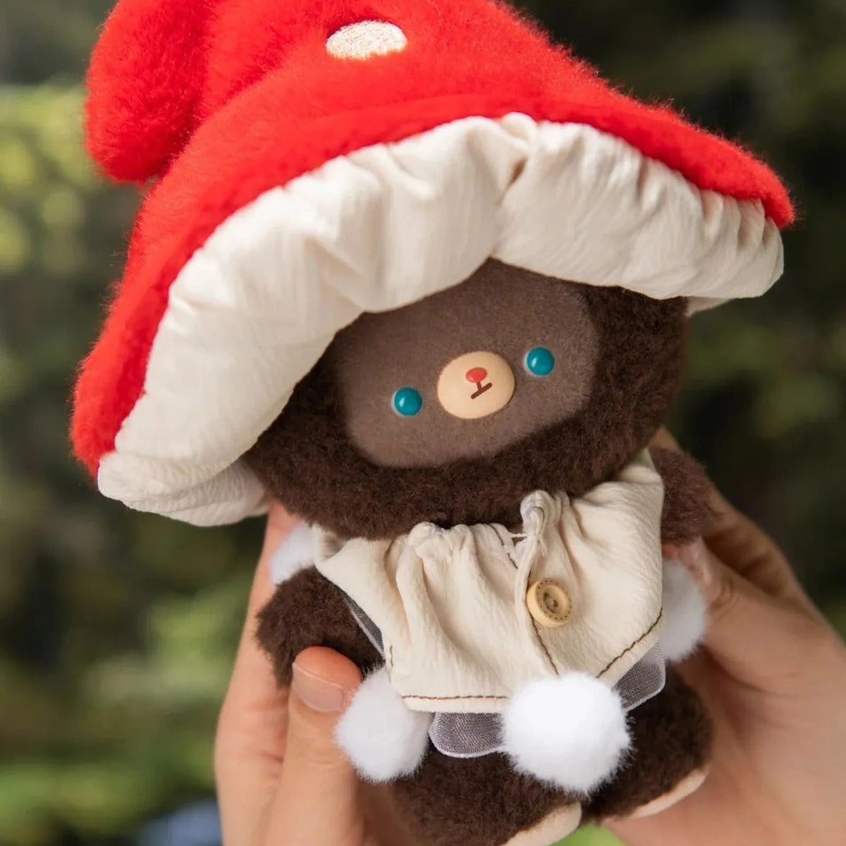 KUMARU Fairy Tale Town mushroom-hat plush shown in a hand, with cream cape and white pom-pom details