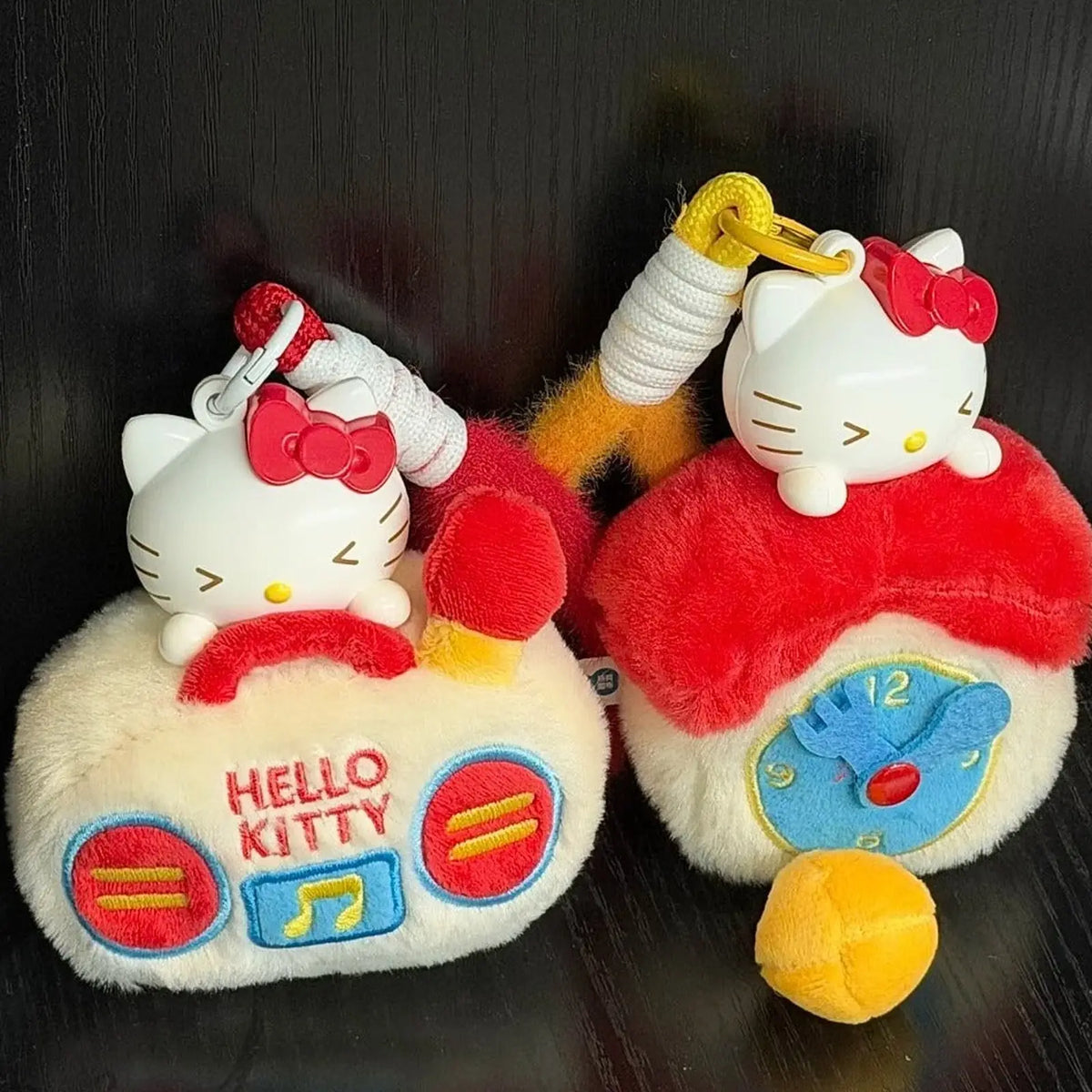Hello Kitty clock- and retro-radio-shaped plush charms on a dark surface; design examples, not guaranteed blind-box contents