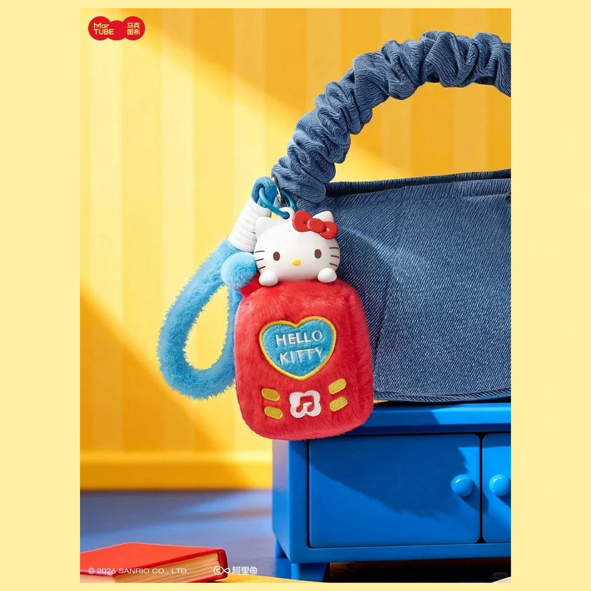 Hello Kitty red music-player-shaped plush charm displayed on a blue handbag; original factory/copyright marks retained; bag and scene props are not included contents