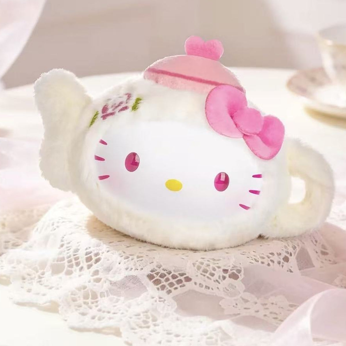 Pink teapot-shaped plush design example on lace; display props are not promised as included