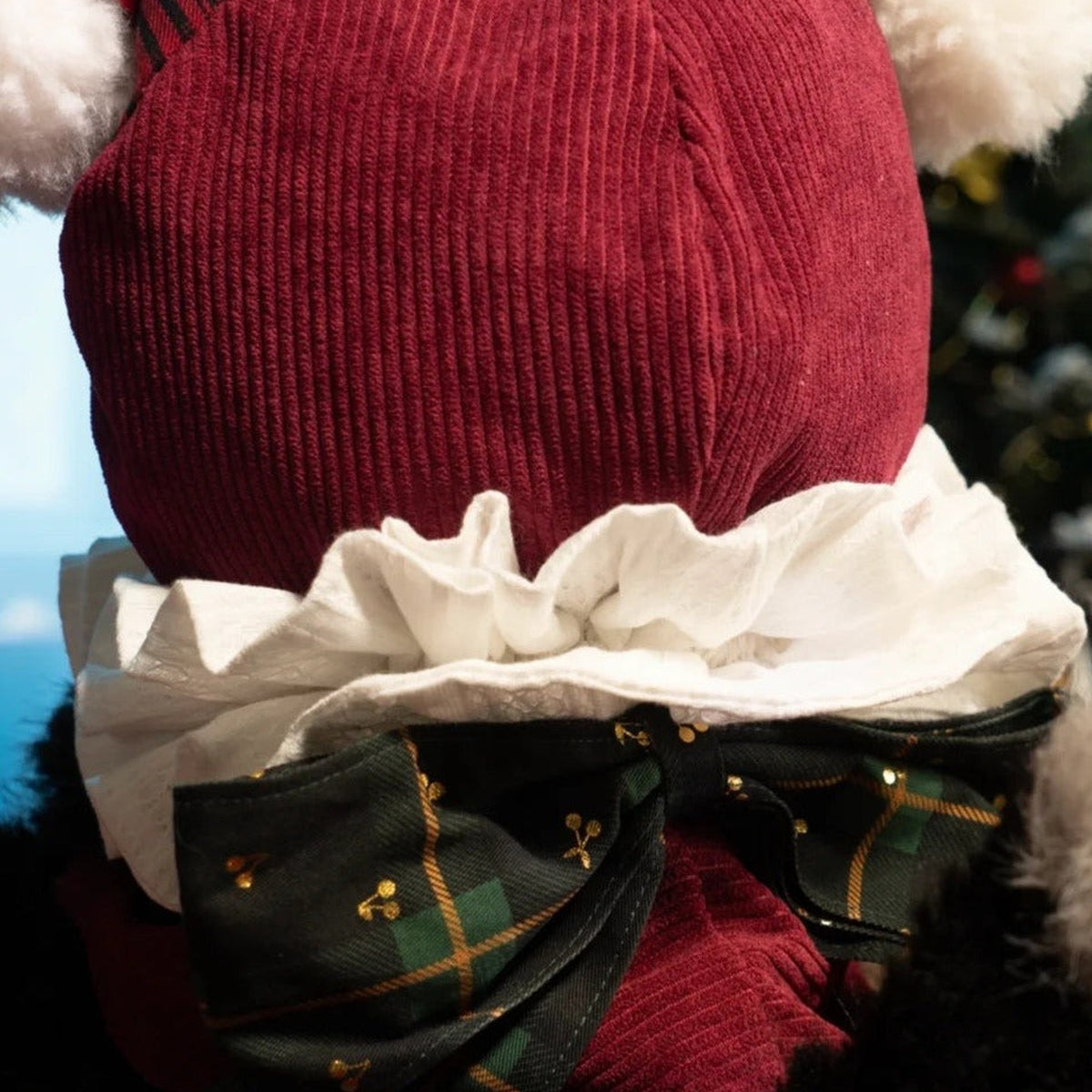 Rear close-up of MayMei Christmas Gift plush showing knitted hood, white ruffle collar and plaid bow