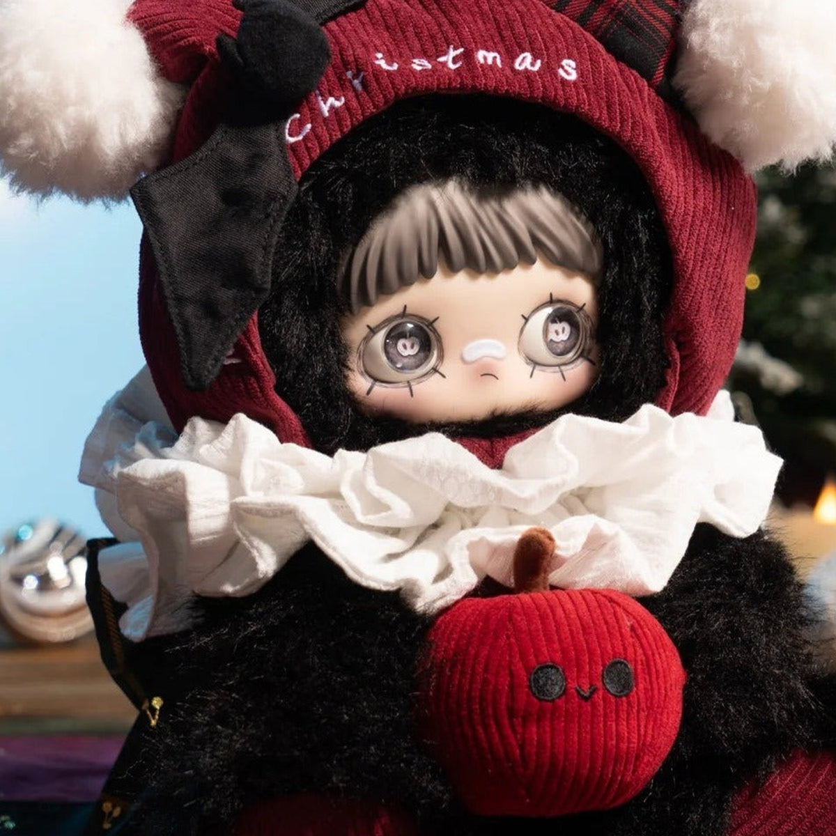 Close-up of MayMei Christmas Gift plush showing face, white ruffle collar and red apple-shaped front detail