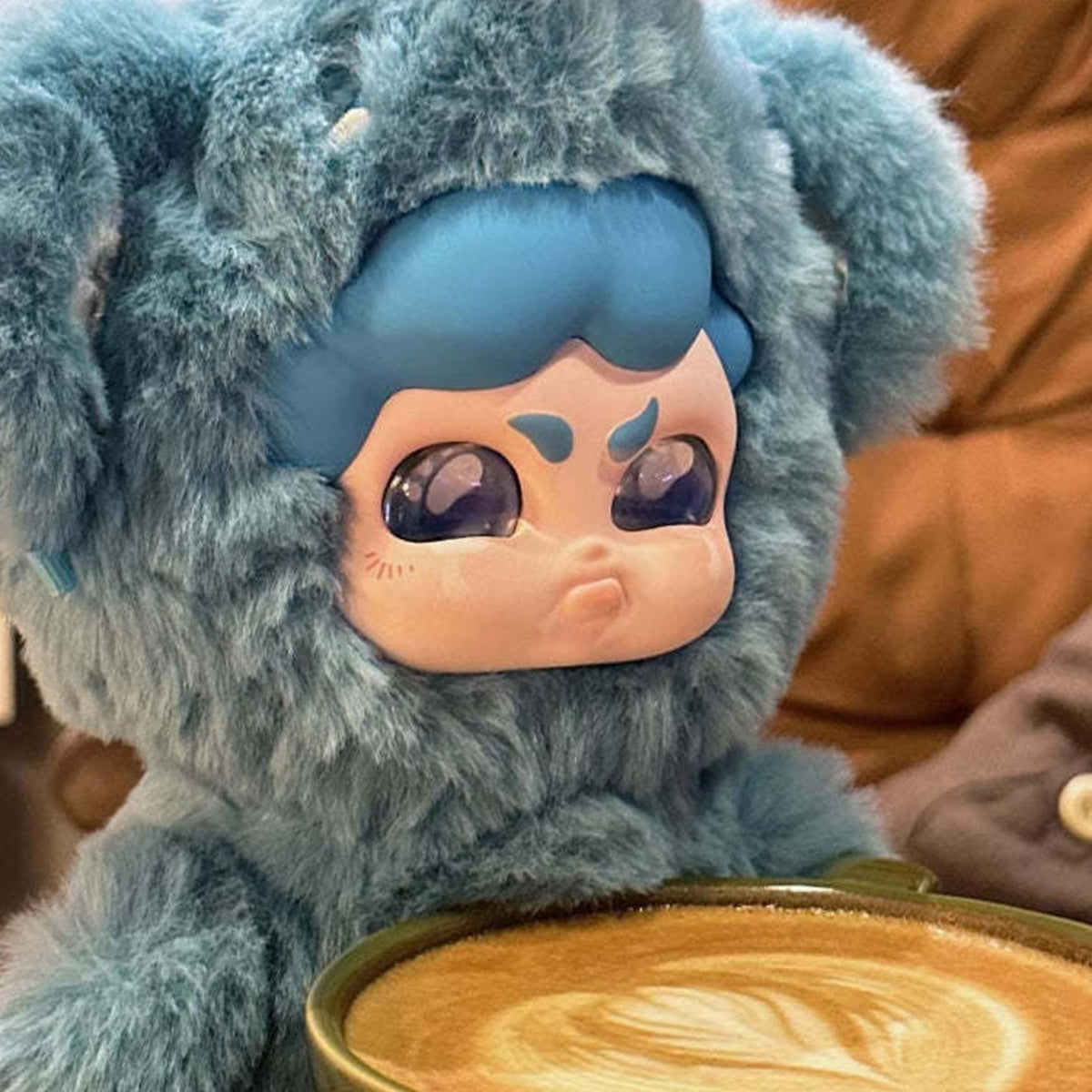 MUMU FOREST WHISPER Series Plush Dolls, Blind Box - Blue MUMU plush face and hood detail at a coffee table; upper tuft cropped and lower body obscured by cup; random design not guaranteed; display props not included
