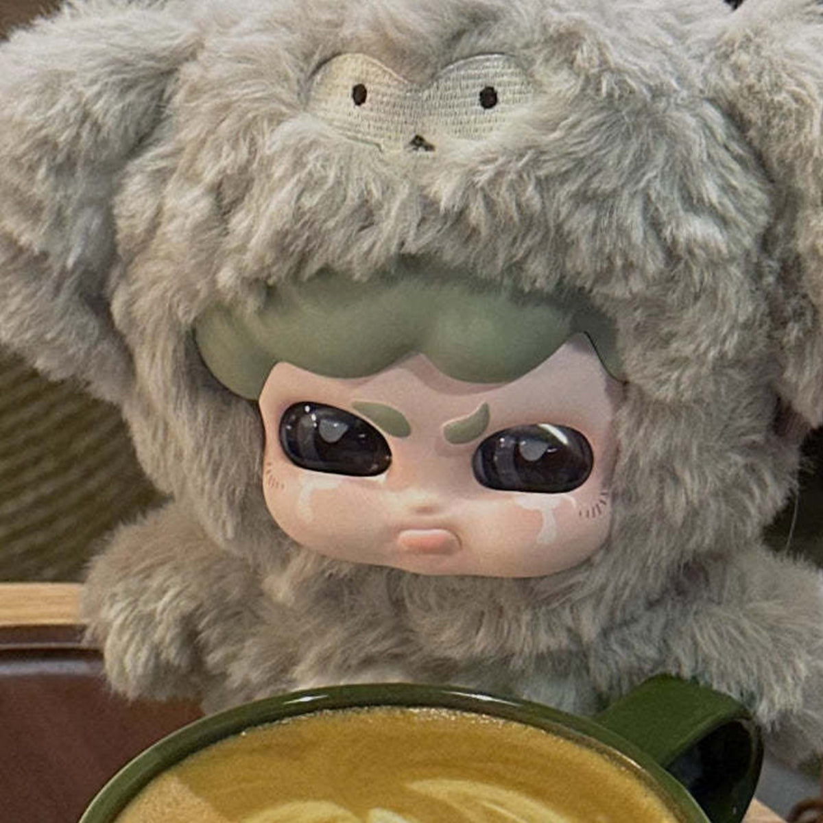 MUMU FOREST WHISPER Series Plush Dolls, Blind Box - Gray MUMU plush hood and face detail behind a coffee cup; upper hood and lower body cropped or obscured; random design not guaranteed; display props not included