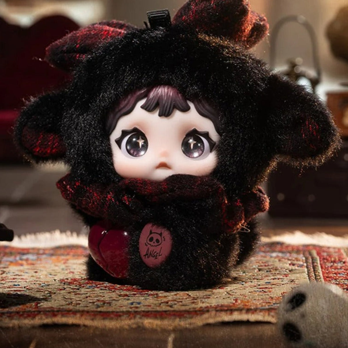 NOMMI x HEYMI Saint? black plush doll with dark red scarf, heart ornament and pink belly patch in a display scene