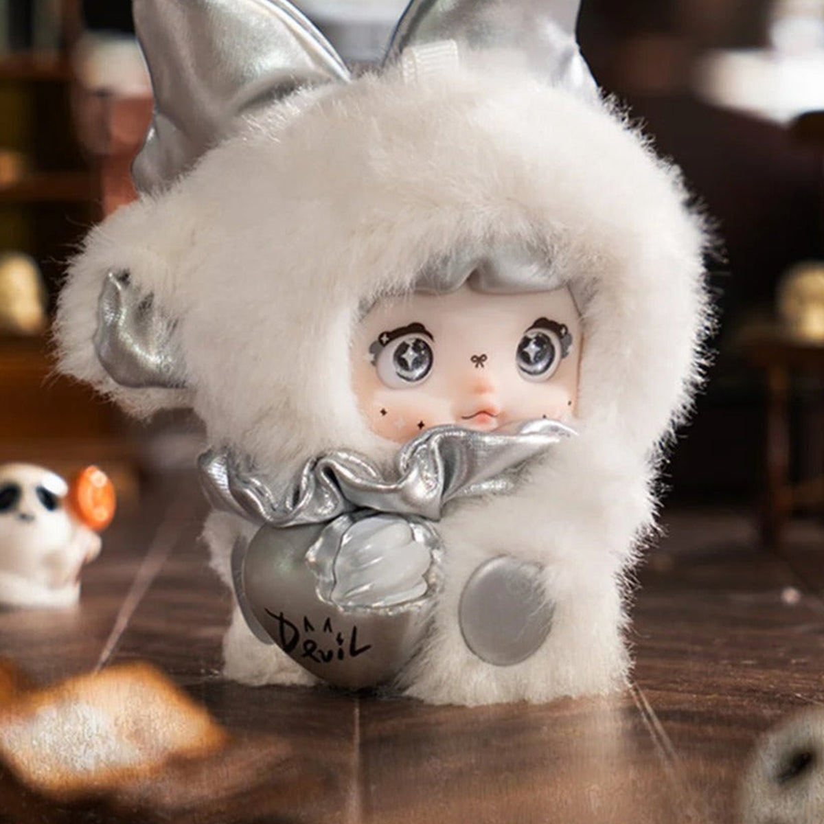 NOMMI x HEYMI Sin? white plush doll close-up showing gray fringe, silver bow and Devil heart ornament