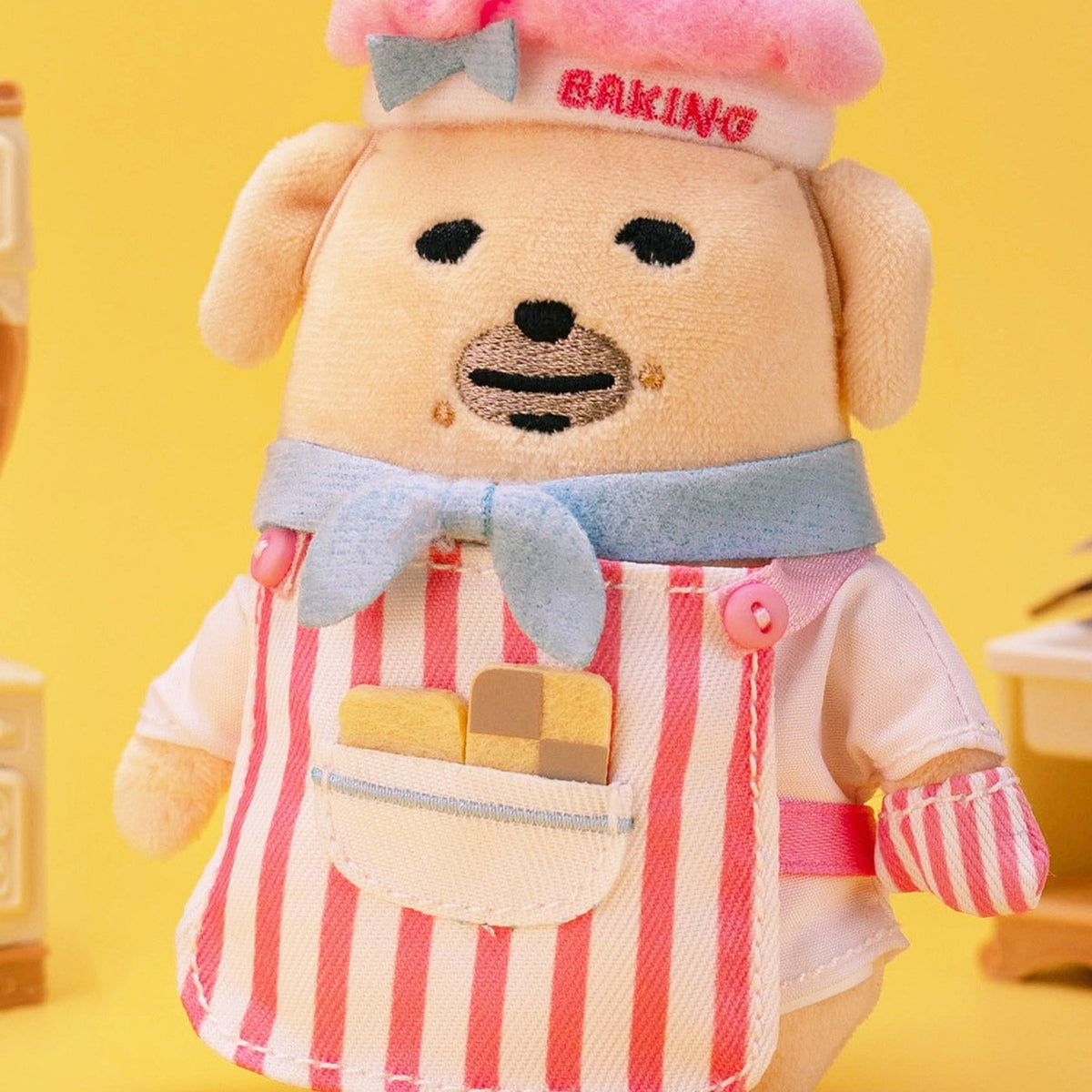 Nudaeng Baking Chef Dog plush pendant: front view of blue bow, striped apron and oven mitt